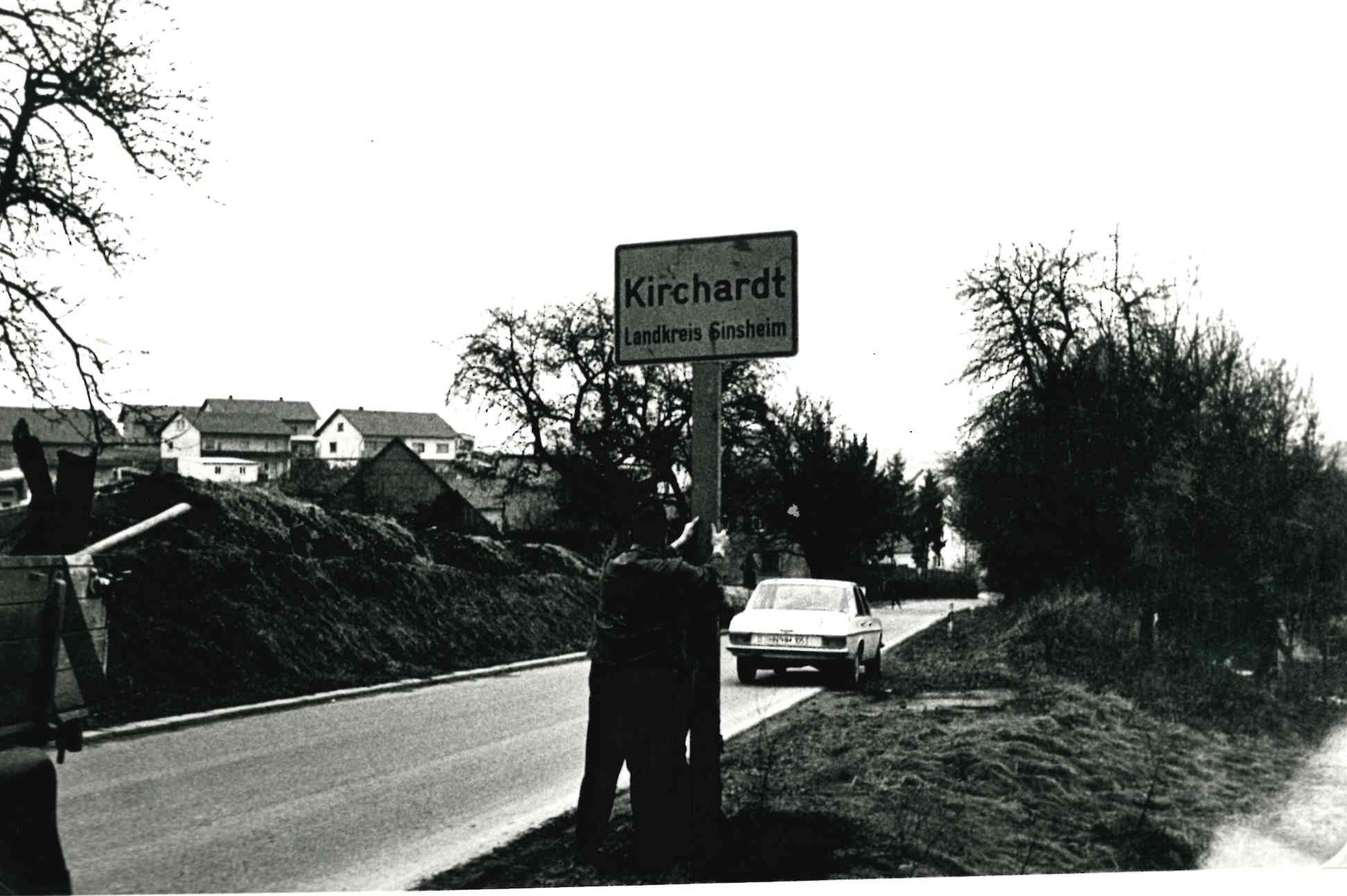  Zwei Gemeindearbeiter gemontieren das alte Ortsschild, auf dem noch &quot;Kirchardt - Landkreis Ssinsheim&quot; steht. Im Hintergrund ein parkendes Fahrzeug am Straßenrand und erste Häuser des Ortes links im Bild. - Das Bild wird mit Klick vergrößert Das Bild wird mit Klick vergrößert 