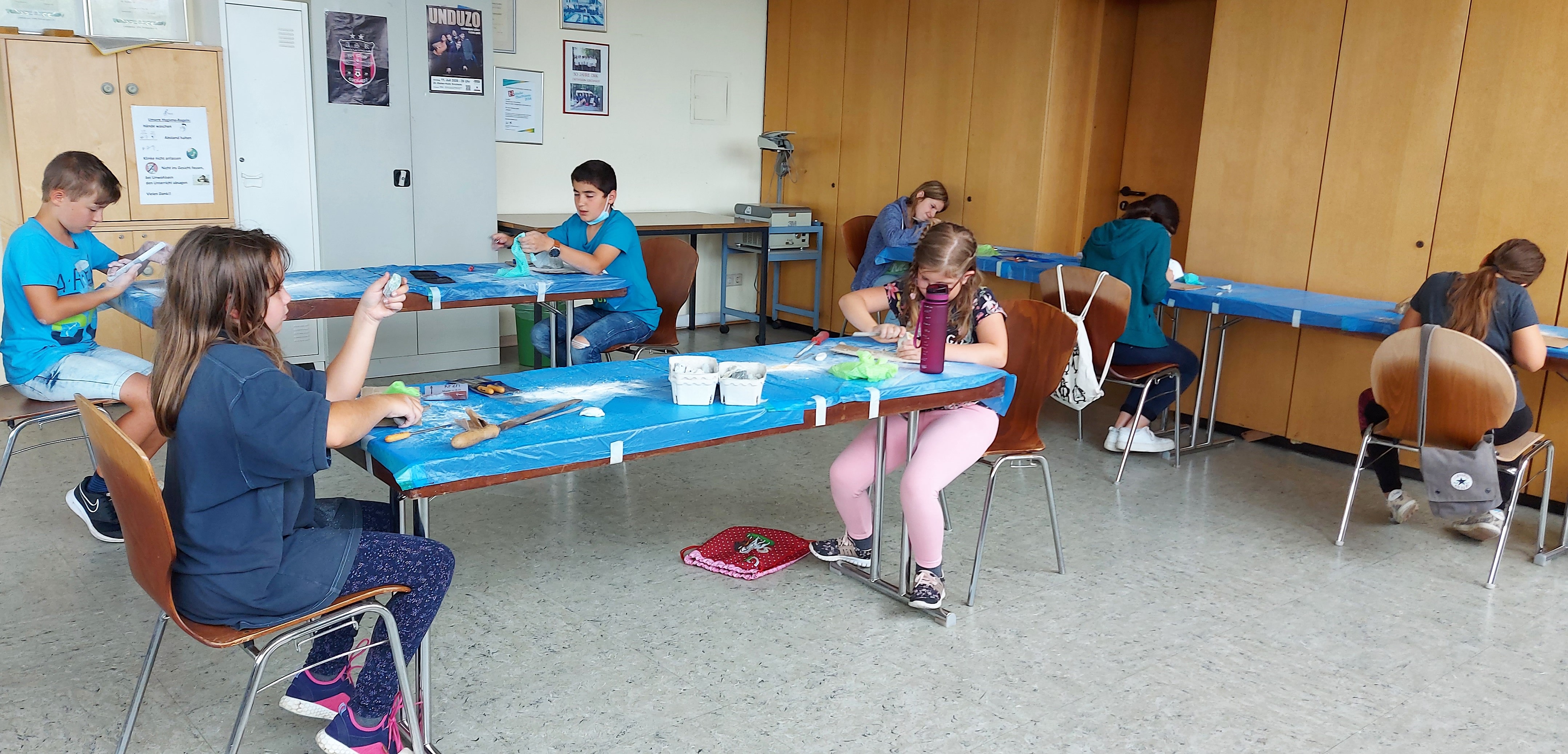 Die Kinder, die an mehreren Tischen verteilt sitzen, bearbeiten die ausgesuchten Specksteine mit Feilen. - Das Bild wird mit Klick vergrößert 