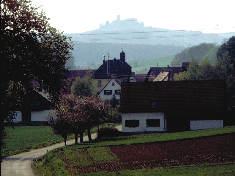  Grüne Felder, blühende Bäume, Häuser von Bockschaft. Im Hintergrund ganz blass die Burg Steinsberg in Sinsheim-Weiler zu erkennen. - Das Bild wird mit Klick vergrößert. 