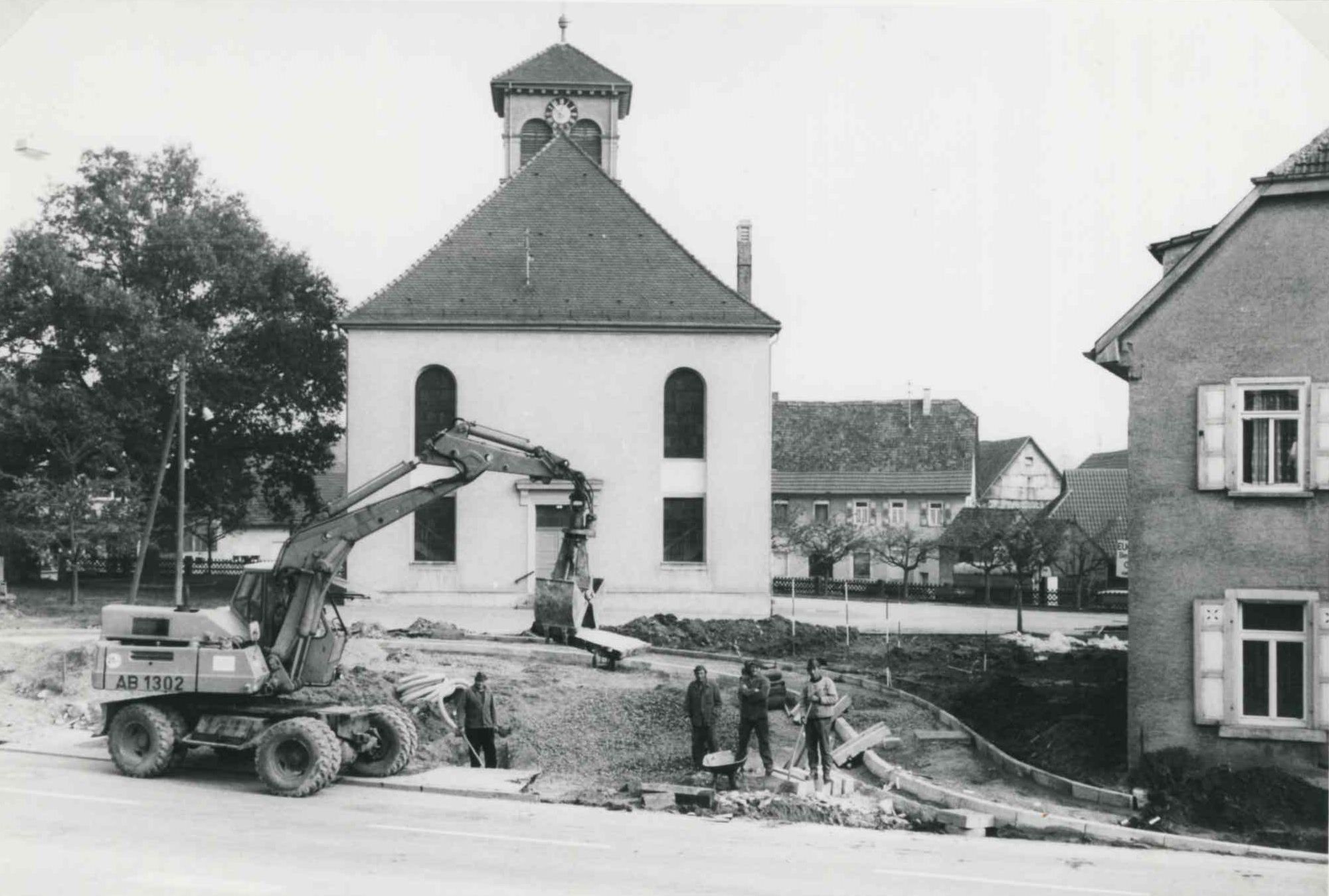  Ein Bagger und mehrere Bauarbeiter stehen vor der Berwanger Kirche. Ein Fußweg wird neu angelegt. - Das Bild wird mit Klick vergrößert 